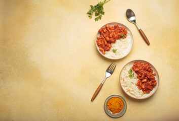 Indian chicken curry with rice and turmeric on yellow background with copy space top view