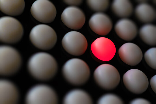 Primer plano de cuadr&iacute;cula de esferas blancas con una esfera roja iluminada destacando en el centro.singularidad y contraste, simbolizando individualidad, ruptura y poder del &eacute;nfasis visual.