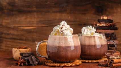 Two glasses of hot chocolate with whipped cream on rustic wooden background