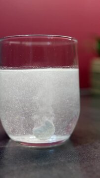 Soluble aspirin pill fizzing and releasing bubbles in a glass of water. Healthcare and medical concept for treating headache or pain