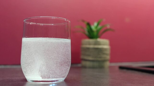 Clear effervescent tablet dissolves effortlessly in a glass of water, creating bubbles for relief from pain and hangovers