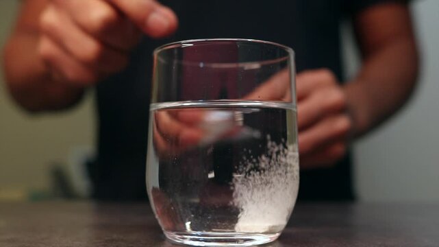 White effervescent tablet dissolving in a glass of water, releasing bubbles. A person drops the pill to cure a headache or hangover