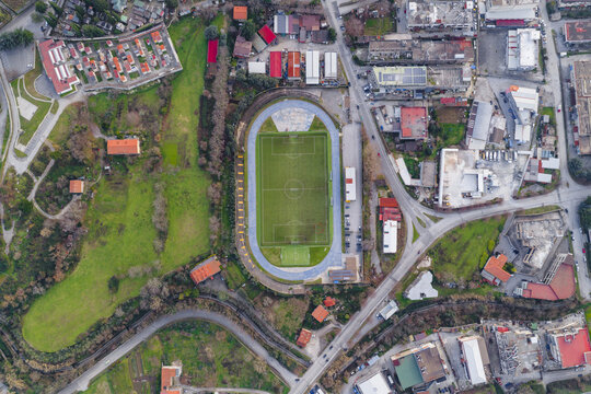 Aerial view of an emerald green football field embraced by a cobalt running track, nestled amid the tanning factory buildings and verdant hills, Solofra, Campania, Italy.