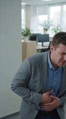 Fototapeta premium A man in an office appears to be in discomfort, holding his stomach, suggesting a potential health issue or stress-related reaction.