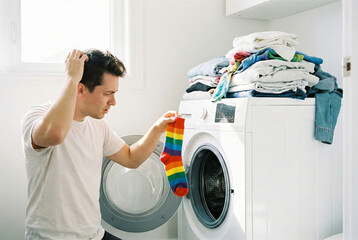 Man holding colorful socks in front of an open washing machine in a bright laundry room