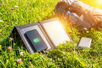 A portable solar panel charging a smartphone in a lush green meadow on a sunny day from a high angle