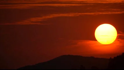 Fotobehang Rood paars Dramatic sunset over mountain silhouettes in South Korea, with a glowing sun and warm orange sky. Natural landscape scene symbolizing tranquility, nature and the beauty of the Asian countryside.  © benny