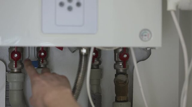 Man pointing to pipes with red taps of the heating gas boiler. 4K