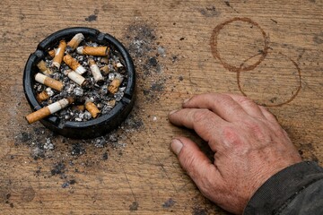 Smoldering Shadows: A poignant composition featuring a brimming ashtray with discarded cigarette butts, a hand resting near it.