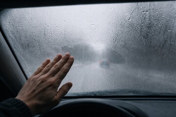 Safety First: Hand wiping condensation on the car windshield during a rainstorm, highlighting the challenge of obscured visibility. Emphasizing the importance of safe driving practices
