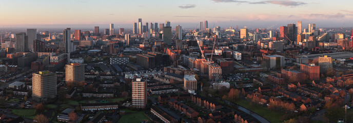Aerial panorama looking southwest from Miles Platting across the Rochdale Canal toward the high-density skyscrapers of Manchester city centre at sunrise.