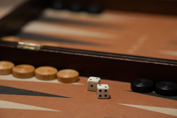 Close-up of backgammon checkers and dice thrown across a traditional wooden backgammon board. Symbol of strategy, luck, entertainment, leisure time, and classic tabletop games