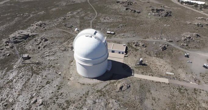 Drone aerial approach to Calar Alto Observatory dome, Tabernas Spain, white telescope building on rocky barren terrain with access road