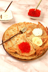 Delicious Russian pancakes with soft cheese, bananas, and red caviar on a marble table. Healthy breakfast with fresh ingredients, Maslenitsa concept and traditional Russian cuisine, selective focus