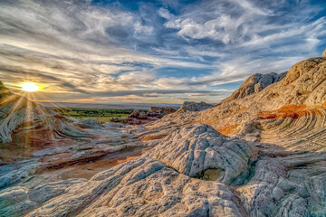 A rocky landscape with a sun setting in the background. The sky is cloudy and the sun is shining brightly