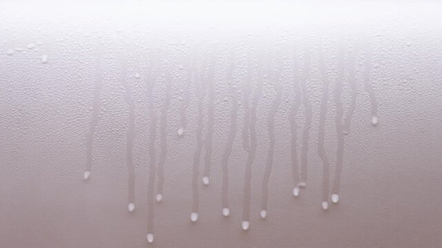 Water droplets trickling slowly down a brightly lit kitchen wall