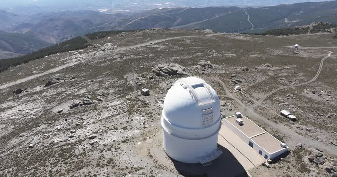 Close drone aerial approach to Calar Alto Observatory dome in Tabernas, Spain, scientific telescope building on rugged rocky plateau