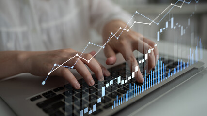 Hands typing on a laptop keyboard create a dynamic financial graph overlay. This image captures the...