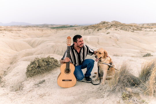 Blind man with guide dog and guitar in desert setting