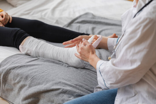 Girl with broken leg and doctor in clinic. Traumatologist orthopedist examines child leg in medical office. Doctor examining girl with medical plaster leg cast after broken ankle injury Rehabilitation