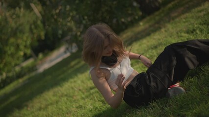 park dancer collapses onto grass after tumble, playful recovery sequence with hair toss and laughter, lounging on sunlit slope with red sneakers and casual top, intimate outdoor calm and candid mood