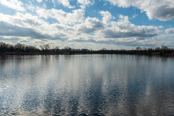 Pond with trees around during partly cloudy springtime afternoon