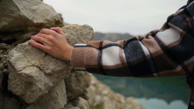 Traveler woman with backpack gently touching stone in mountains, connecting with nature while enjoy freedom and adventure during journey in beautiful landscape with lake