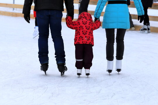 Little child skates at the ice rink in winter. A man and woman is teaching child to skate. Sports clubs, active family sport