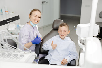 Obraz premium Happy dentist and child patient showing thumbs up in dental clinic