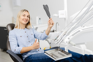 Patient admiring smile after dental checkup using small mirror in modern clinic
