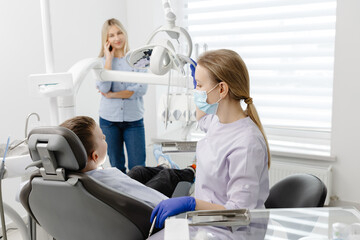 Dentist wearing mask and gloves examining young boy in dental clinic