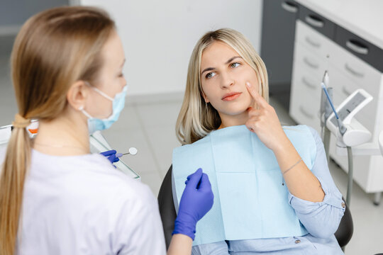 Dentist holding dental mirror and listening to patient describing toothache