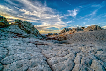 A rocky desert landscape with a blue sky in the background. The sky is filled with clouds, giving the scene a serene and peaceful atmosphere