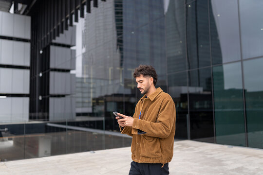 Young man walking outdoors checking smartphone, staying connected in city, urban digital lifestyle