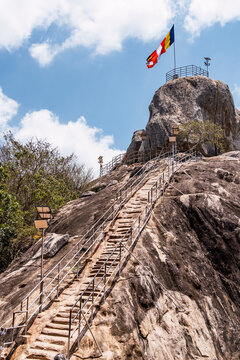 Mihintale rock staircase with flags under blue sky