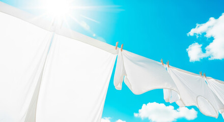 Clean white laundry hanging on clothesline against blue sky and bright sun