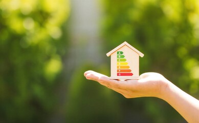 Hand holding eco friendly energy efficiency rating model house