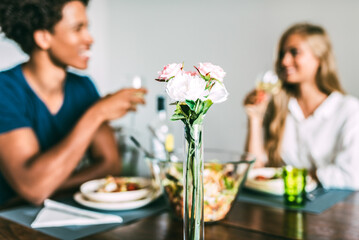 Multiethnic couple enjoying meal at home with focus on flowers