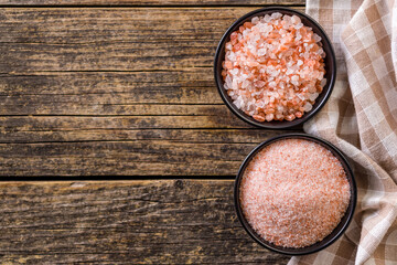Pink Himalayan salt in bowl on wooden table. Top view.