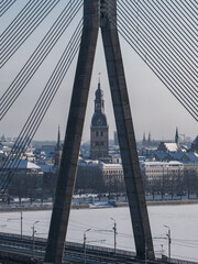 Fototapeta premium Aerial winter scene of Vansu Bridge framing the Riga Cathedral clock tower in Riga, Latvia. Snow covers rooftops and the frozen Daugava River, tram lines run along the bank.