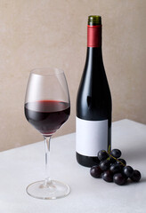 Bottle and glass of red wine, bunch of fresh grapes on light gray table