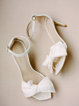 White high-heeled shoes with bows placed on a light background in a simple setting