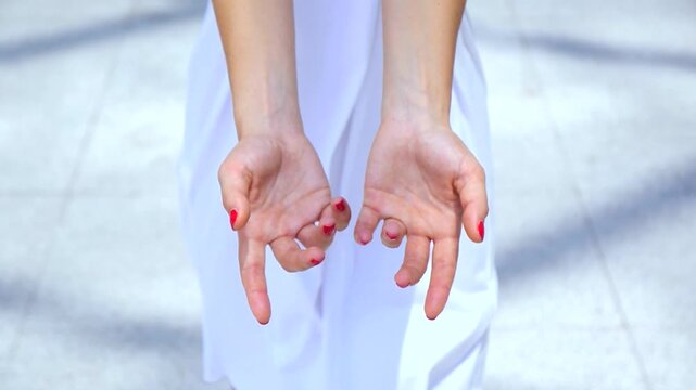 High angle view of a woman's hands with red nail polish wearing a white dress, starting cupped together and full of red rose petals, then slowly opening to let them fall away