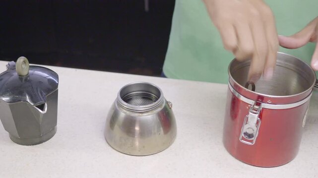 Close-up, high-angle shot of a man preparing coffee. A Latino man fills a personal coffee maker with ground coffee.