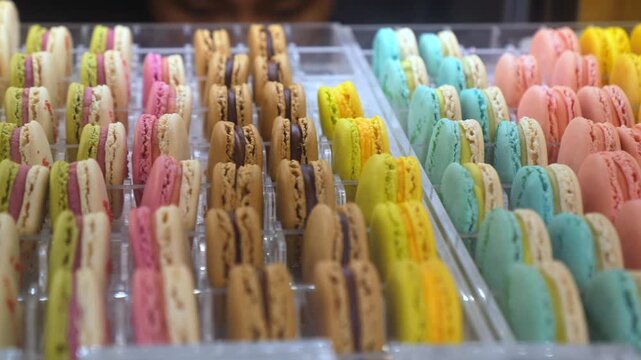 Rows of delicious and colorful french macarons with various flavors standing vertically in a transparent display case inside a bakery, showcasing the delightful and sweet confectionery