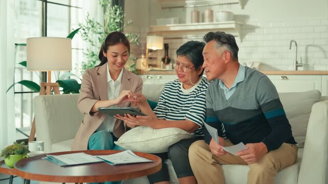  asian female instructor advisor for retirement planning and home insurance senior couple sitting at sofa talking to Female insurance agent financial health retried planing advisor in living room