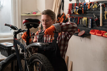 Professional female bike mechanic using screwdriver to fix bicycle seat preparing cycle for new season in workshop