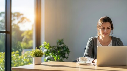 Young professional woman working on laptop in bright minimalist home office with natural sunlight and coffee