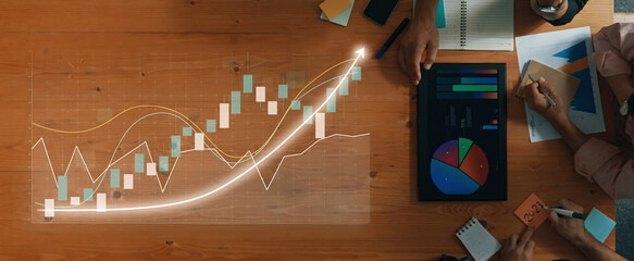 A dynamic workspace showcases hands analyzing financial data through digital graphs and charts on a wooden table, representing collaboration and strategy. Axiom