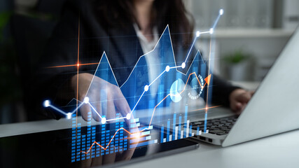 A business professional examines data trends through vibrant graphs and charts on a digital screen while working on a laptop in a modern office setting. Scalp
